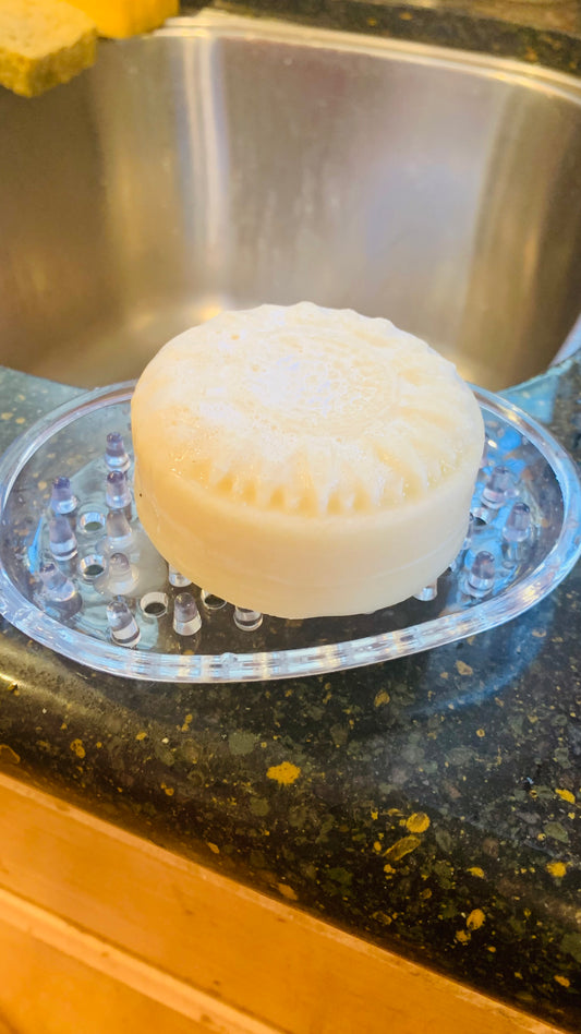 cream colored, solid dish soap bar shaped like a sunflower on a soap dish next to the kitchen sink